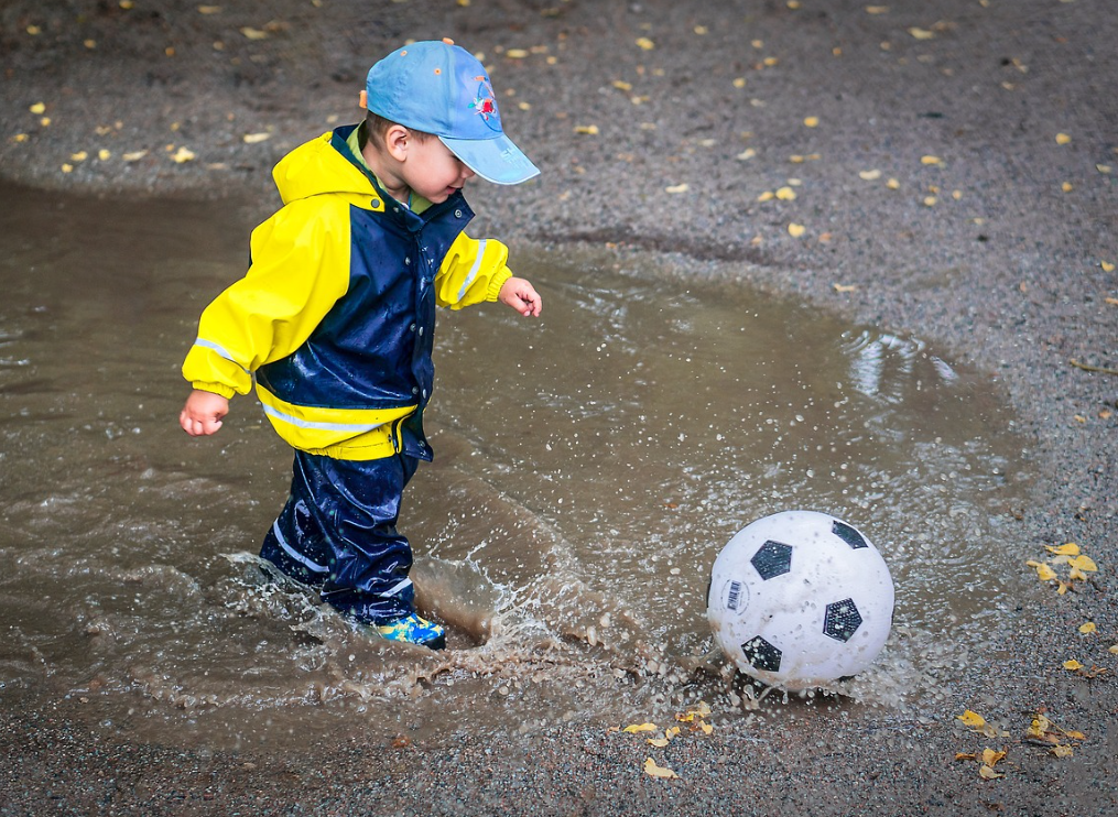 boy in raincoat playing with soccer ball in rainy season